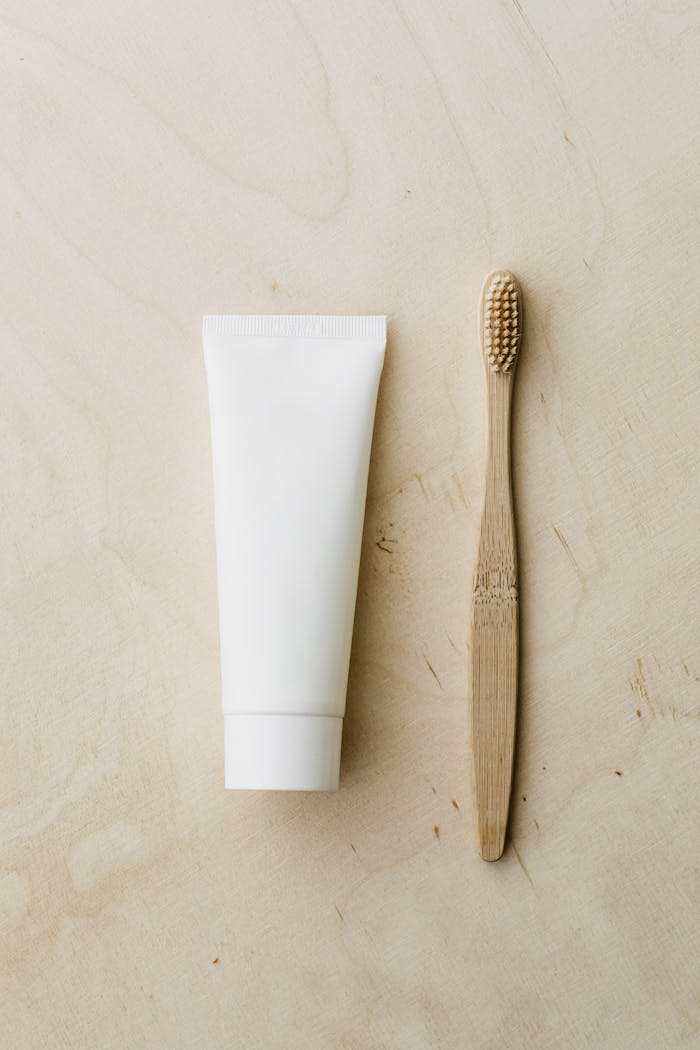 Top view of white mockup toothpaste tube and bamboo toothbrush placed on light brown wooden surface